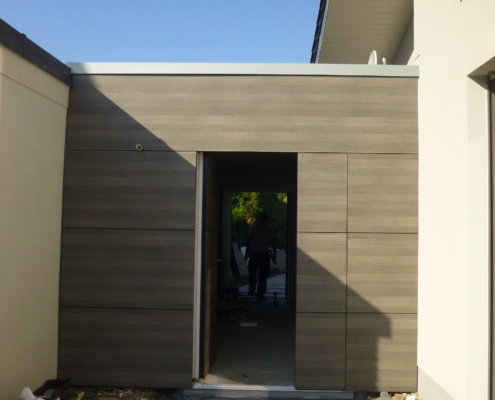 Moderne Fassadenverkleidung mit horizontalen Paneelen an einem kubischen Anbau zwischen zwei verputzten Hauswänden